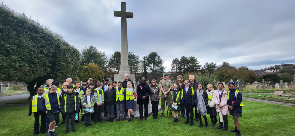 Schoolchildren pose around a cross of sacrifice in an East Sussex cemetery.