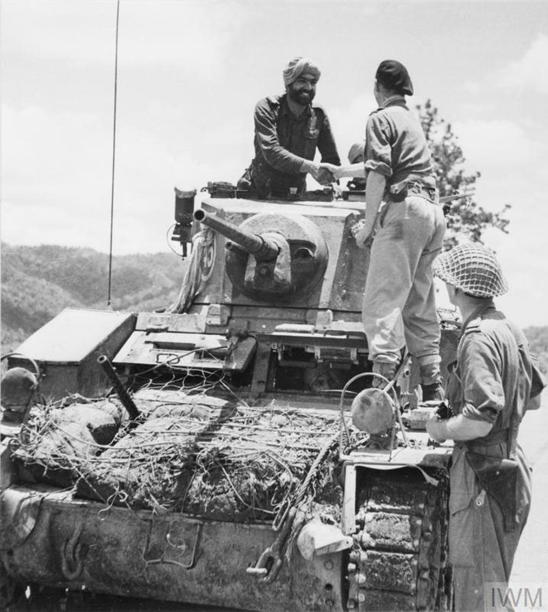 A sikh and British soldier shake hands on top of a tank during WW2.
