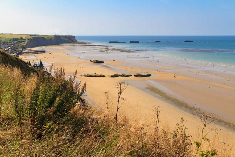 Gold Beach normandy in the present day. The remains of the mulberry floating harbour are visible in the sea and on the beach.