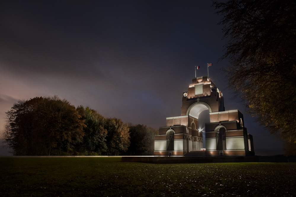 Thiepval Memorial lit up at dusk beneath a dark purple and grey sky.