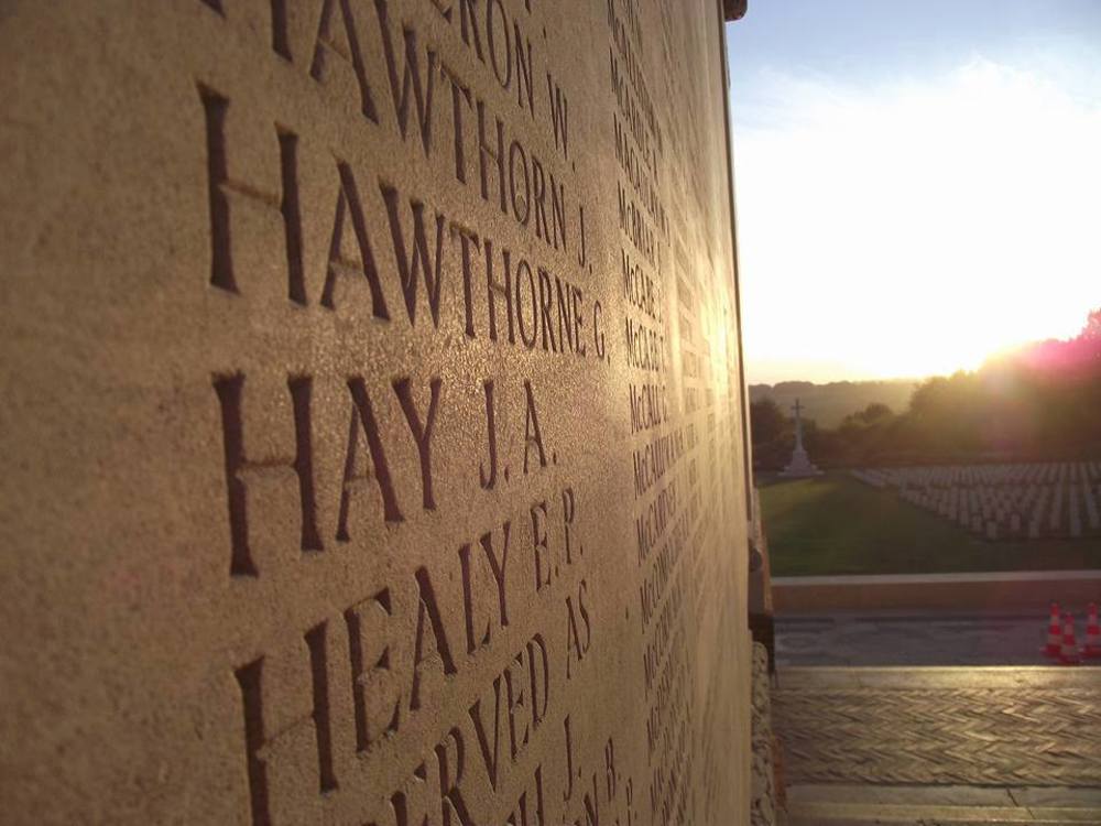 Sun shines on a Thiepval Memorial name panel. You can see several names carved into the stone name panel.