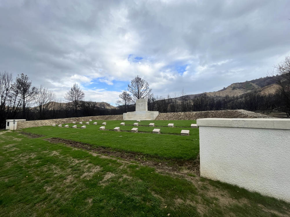 Headstones and memorial set on a green lawn under a cloudy sky in Gallipoli, Turkey.