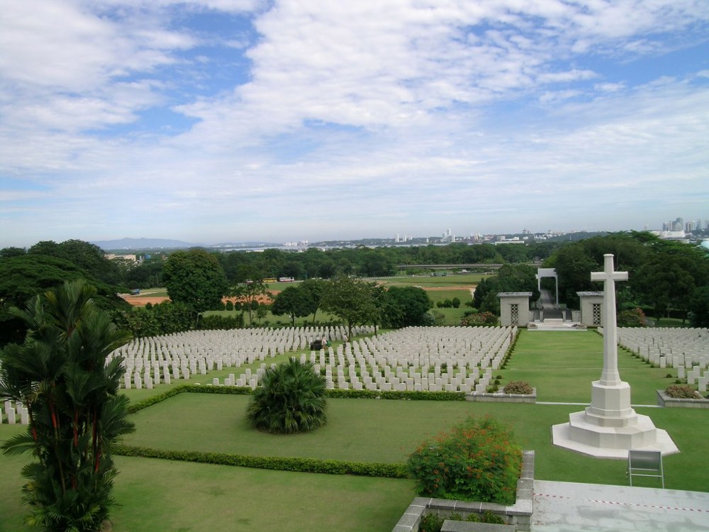 View of Kranji War Cemetery showing rows of sleek white headstones and white cross of sacrifice.