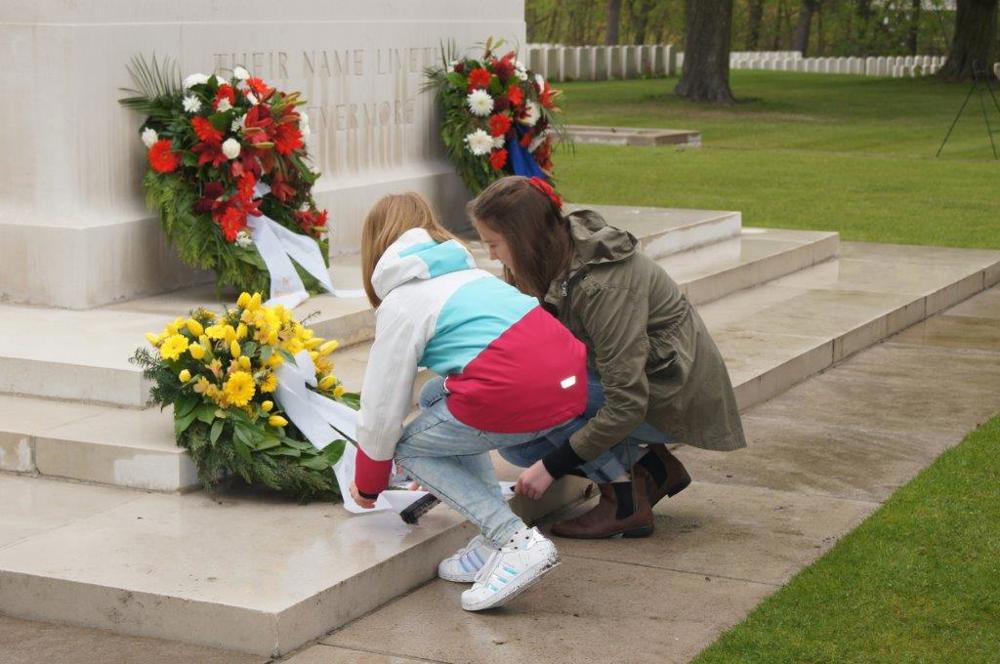 Two girls lay a colourful flower wreath on the steps of the Stone of Remembrance at Berlin War Cemetery.