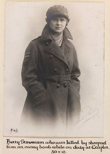 Volunteer Betty Stephenson. She is wearing a bright scarf underneath a thick belted woollen military overcoat. On  top of a short crop of hair sits a military-style driver's cap. She has a round face and wears a stern expression.
