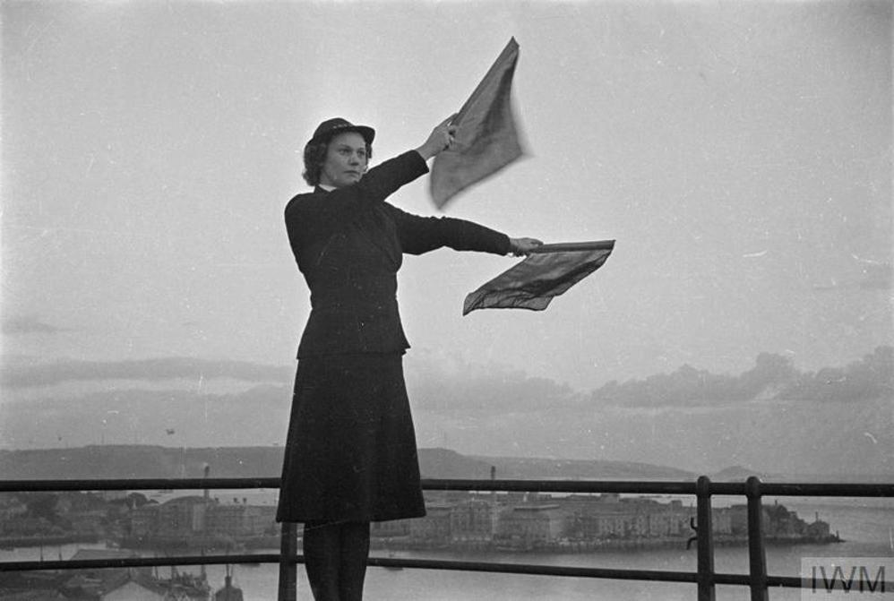 A WRNS member performs semaphore atop a railed, high vantage point.