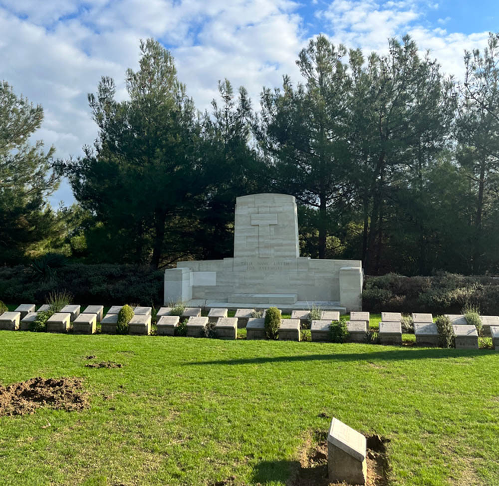 Altar-like Stone of Remembrance in white stone with carved cross sits behind two low rows of CWGC grave markers at Johnston's Jolly Cemetery, Gallipoli.