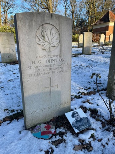 Headstone of Trooper Harry George Johnston. Headstone features a carved Canadian maple leaf set above the following text: M.8053 Trooper H.G. Johnston 1st Armoured Personnel Carrir Regiment 17th January 1945 Age 29. The text sits above a carved cross. Beneath the cross reads the following inscription: Gone but not Forgotten