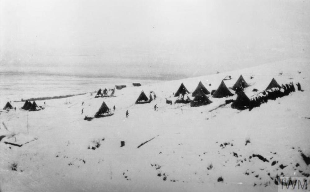 Snow coverd huts and tents of the British Army dot a snow-covered hillside.