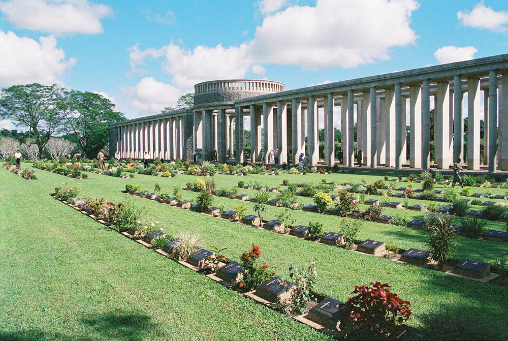 War graves decorated with flowery blooms lie in front of the Rangoon Memorial at Taukkyan War Cemetery.