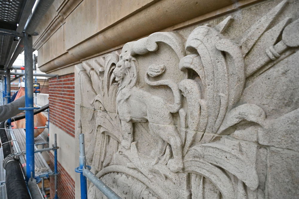 Close up of decorative masonry on the Menin Gate, showing a lion carved in stone over a triumphal flowers and weaponry motif.