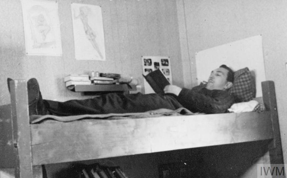 A WW2 Prisoner of War relaxes reading his book on his bunk somewhere in a German prison camp.