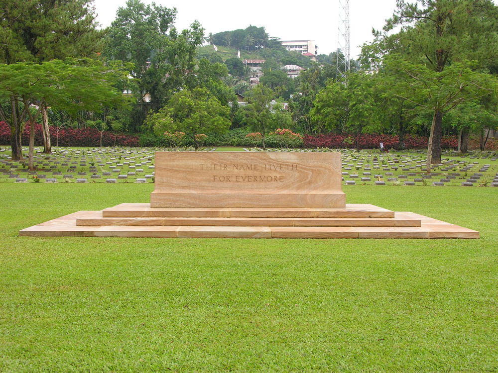 Brown marble Stone of Remembrance sitting in front of war graves plots at Ambon War Cemetery