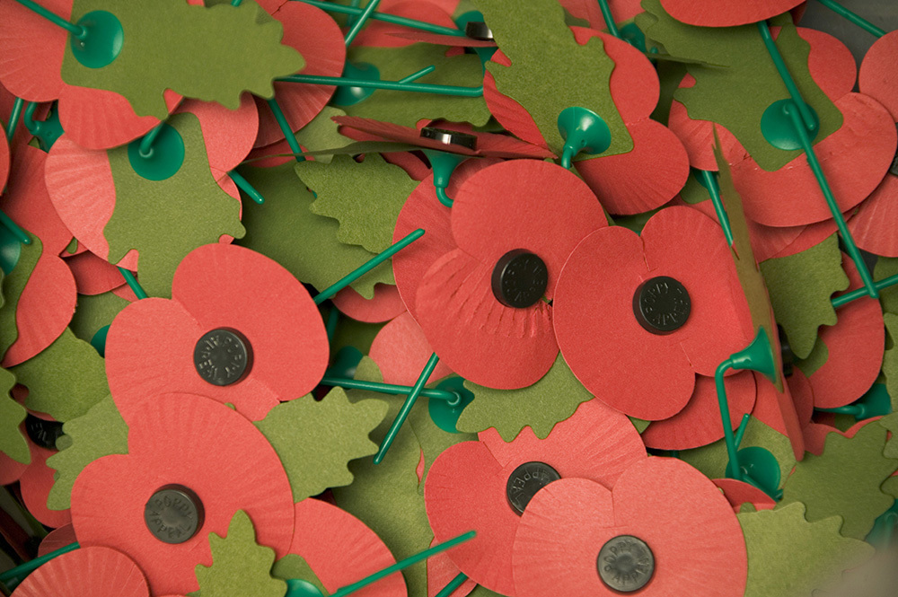 Close up of a pile of old style red RBL poppies with green card leaf and green plastic stems.