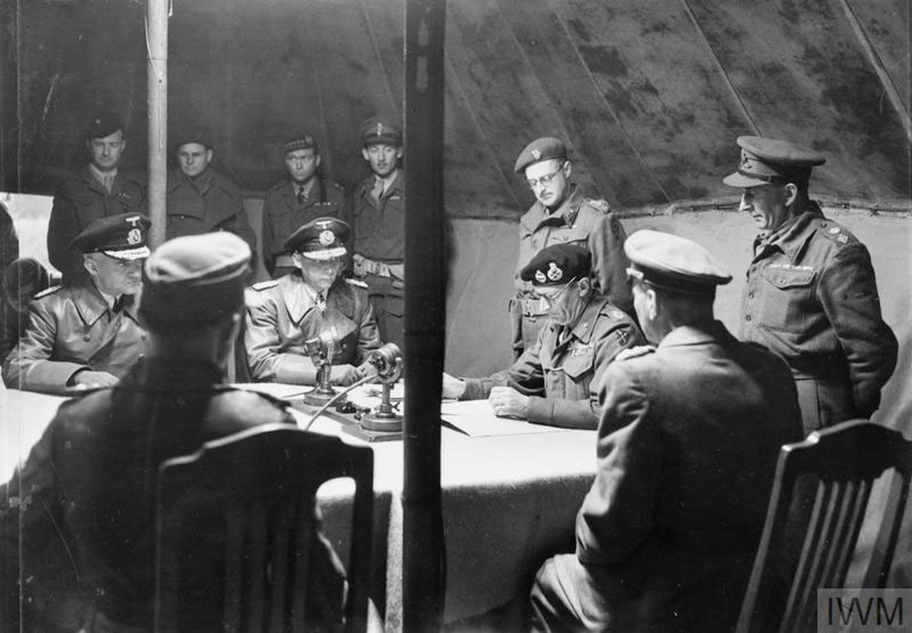 German generals and senior British military staff, including FIeld Marshal Montgomery, meet to sign the official German surrender in May 1945. The German delegation is seated alongside Monty and two other brits, while British officers stand around the negotiating table.