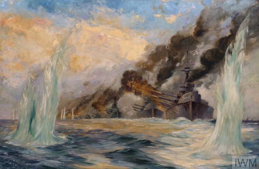 A line of Royal Navy battleships, sailing directly towards the viewer, fire broadsides of artillery fire to the left from their starboard sides during the Battle of Jutland. Large clouds of black smoke rise skywards from the guns and funnels of the ships. Two large plumes of water in the immediate foreground display the effects of German naval gunfire.