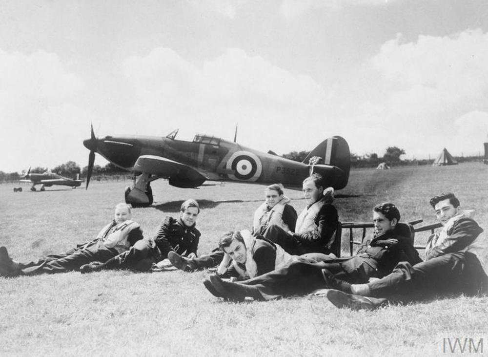 Battle of Britain Pilots sat on grass in front of their Hurricane aircraft.