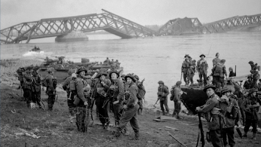 British soldiers exiting their amphibious landing craft after crossing the River Rhine in March 1945. A smashed road bridge is visible in the background.