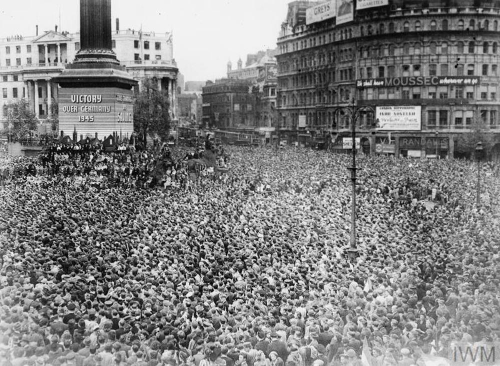 Crowds of people gathered in Trafalgar Square listen to the VE Day announcement on a public PA system,