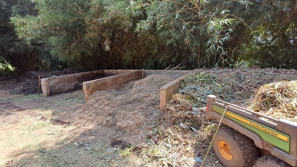 Brick compost bin at a CWGC Kenyan war cemetery. The bin is made of three seperate pens, each bordered by a brick wall. A wagon loaded with compost and garden waste is visible in the foreground.