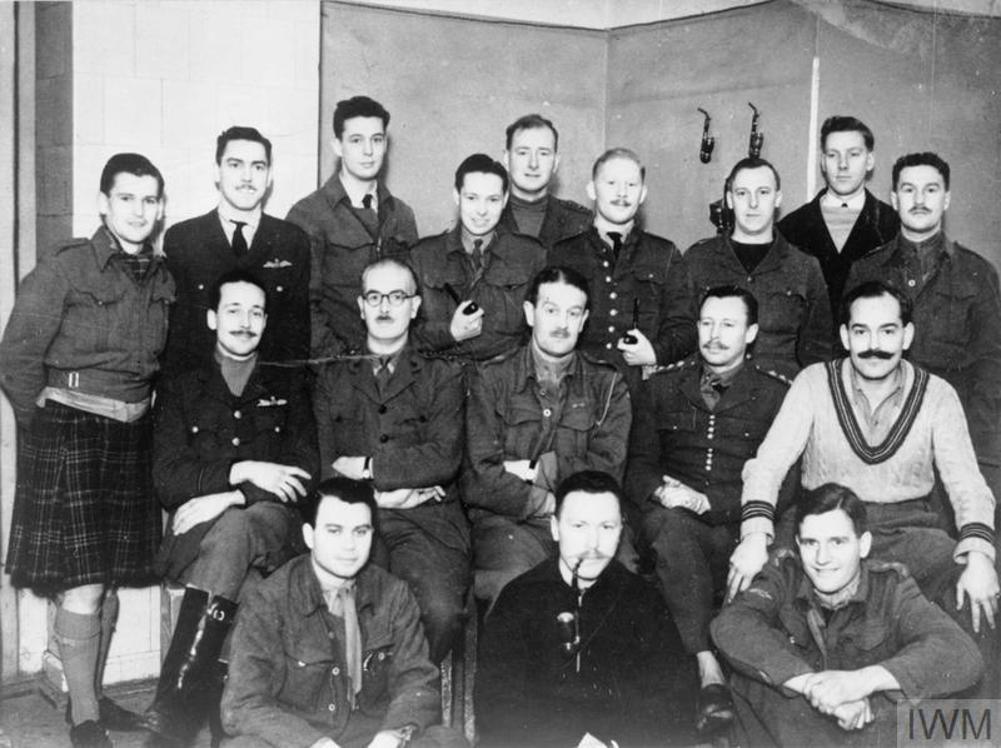 Group photograph of British POWs taken at Colditz Castle. From left to right, first row - Captain Richard Howe, Captain Patrick R. Reid (Escape Officer), Lt Allan (in kilt). Second row - Captain Berry, Captain Elliott, Lt Col German, Padre Platt.