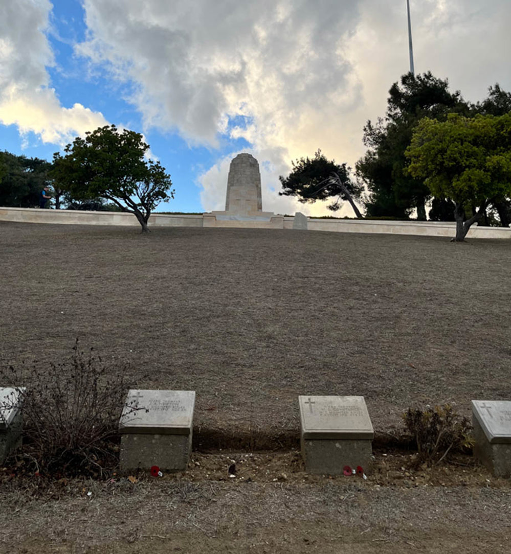 The Chunuk Bair memorial with its central tall rectangular monument and wide curtrain wall as seen from the bottom of a hill in Chunuk Bair War Cemetery.
