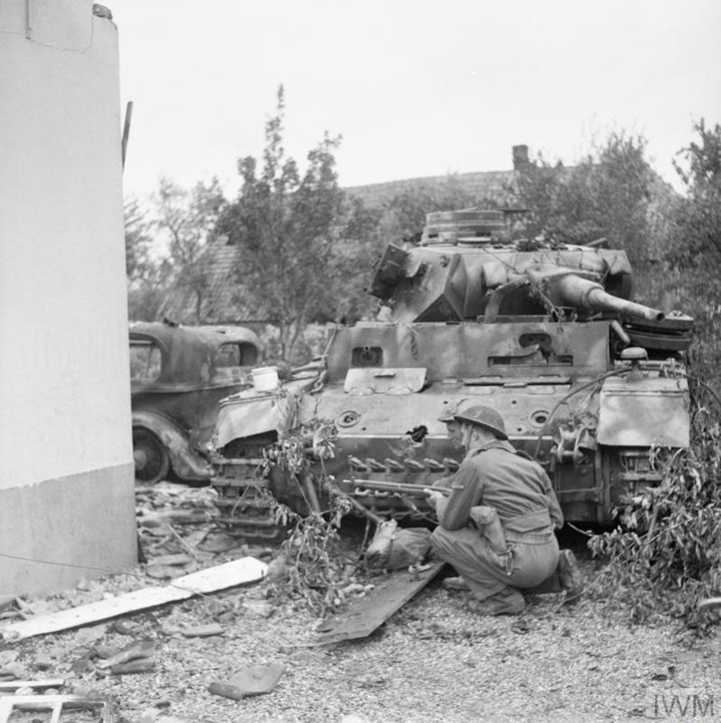 A british soldier kneels behind a destroyed German tank at the Battle of Arnhem